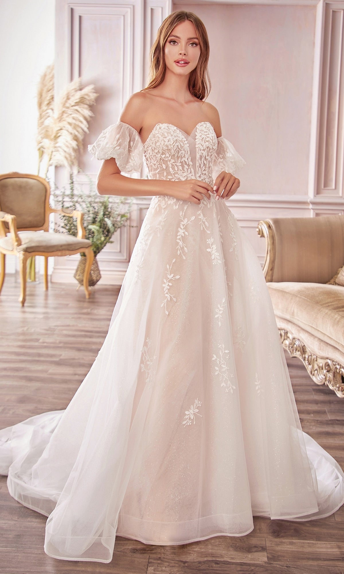 A woman stands indoors wearing the Puff-Sleeve Long White Wedding Dress A1014, featuring off-the-shoulder design, floral lace details, removable puff sleeves, and a long tulle train.